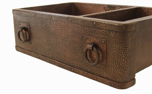 Close-up of a rustic hammered copper double bowl farmhouse kitchen sink with medieval-style rivets and a beautiful apron front.