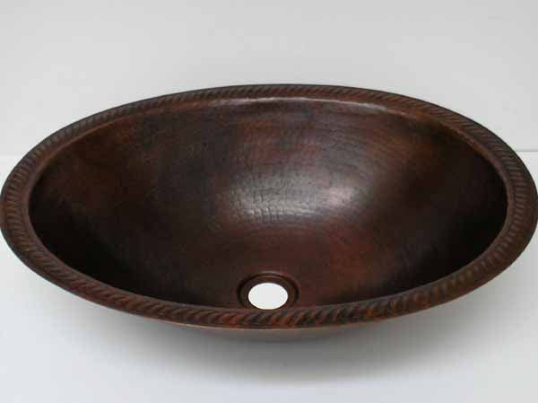 Hand-hammered oval copper bathroom sink with intricate engraved rim detail, showcasing a dark brown finish.